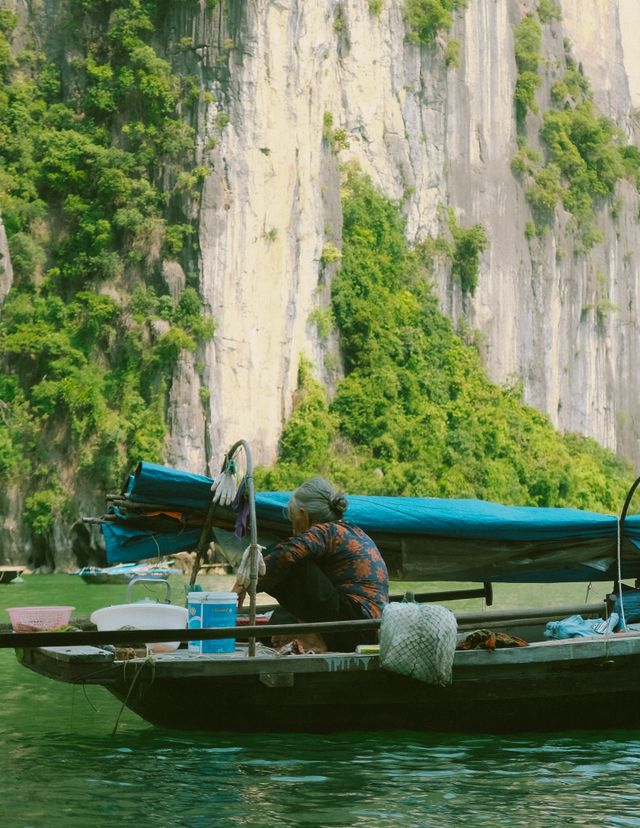 Elderly woman boating on a serene lake against a lush, rocky backdrop.