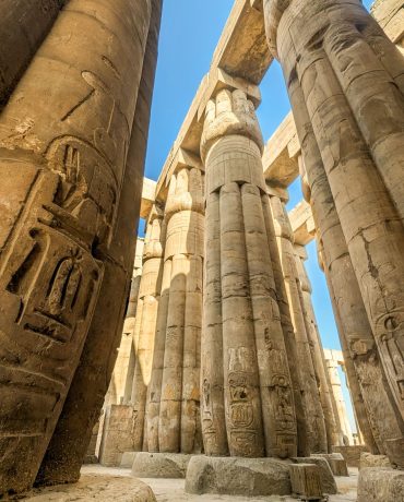 Explore the impressive stone columns of an ancient Egyptian temple under a clear blue sky.